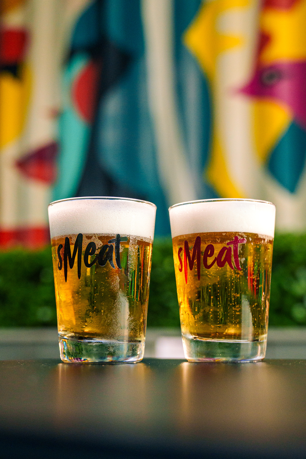 Dois chopps em copos do Smeat, com o mural colorido ao fundo
